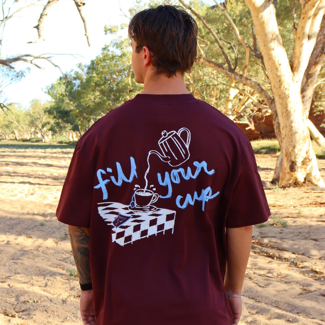 person wearing oversized tee in burgundy with graphic design on the back.